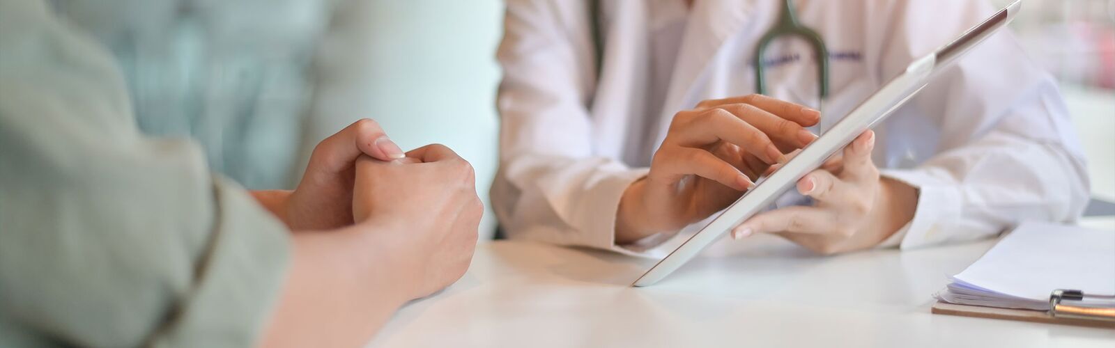 Arzt spricht mit einem Patient / einer Patientin am Tisch und hält ein Tablet in der Hand